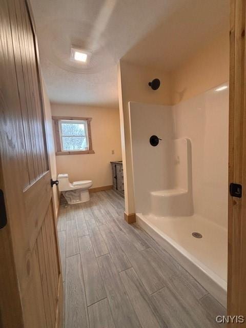 full bath featuring baseboards, a shower stall, toilet, and wood finished floors