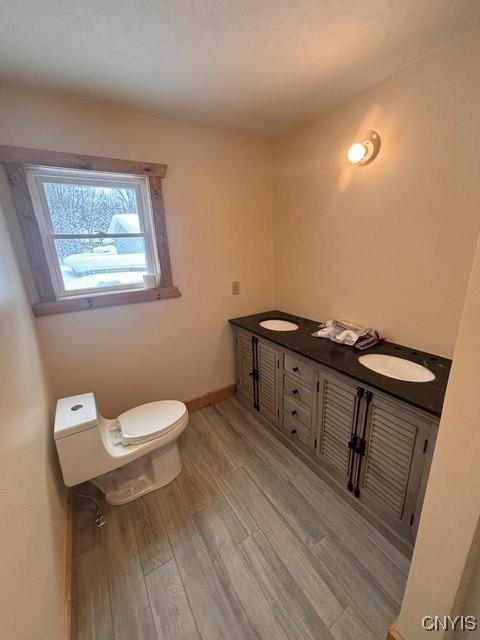 bathroom with double vanity, toilet, a sink, wood finished floors, and baseboards