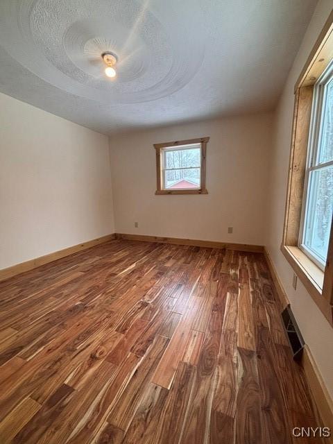 empty room with a textured ceiling, wood finished floors, visible vents, and baseboards