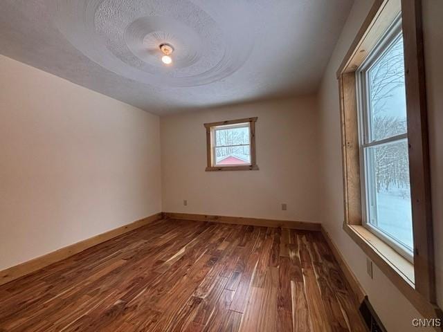 unfurnished room with a textured ceiling, wood finished floors, visible vents, and baseboards