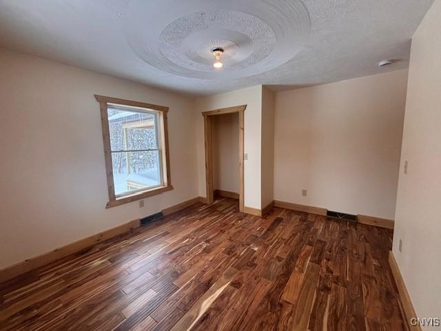 unfurnished bedroom featuring visible vents, a textured ceiling, baseboards, and wood finished floors