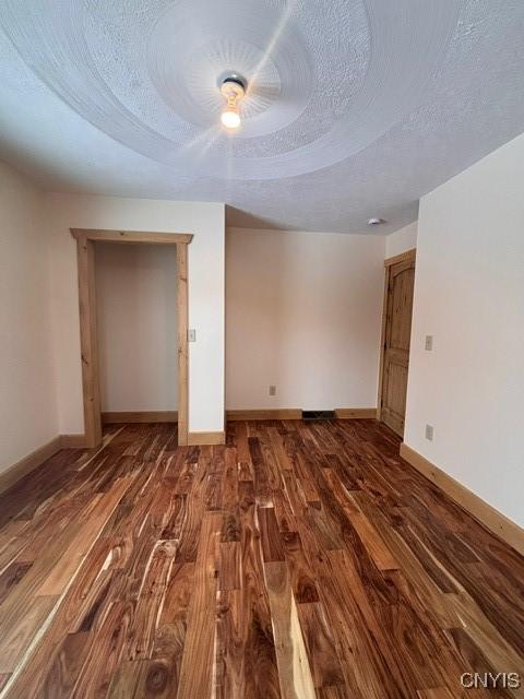 unfurnished room featuring a textured ceiling, baseboards, and wood finished floors