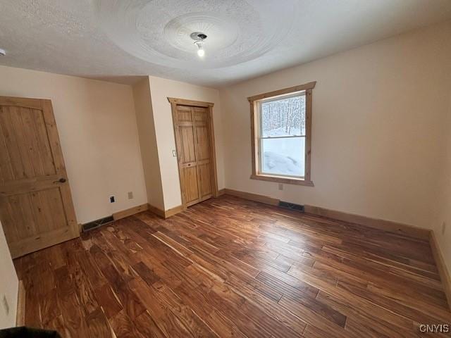 unfurnished bedroom with visible vents, a textured ceiling, baseboards, and wood finished floors