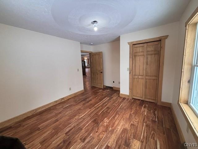 unfurnished bedroom with a textured ceiling, wood finished floors, and baseboards