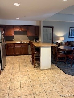 kitchen with light tile patterned flooring, sink, a kitchen bar, and stainless steel fridge