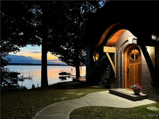 exterior entry at dusk featuring a water view and a yard