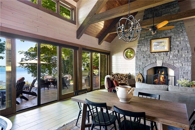 dining room featuring ceiling fan with notable chandelier, hardwood / wood-style floors, wooden ceiling, beam ceiling, and a fireplace