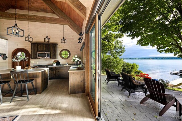 interior space featuring hanging light fixtures, dark brown cabinets, a kitchen bar, sink, and a water view