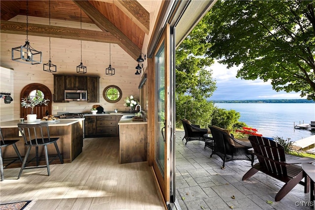 bar featuring stainless steel appliances, a water view, hanging light fixtures, and wood walls