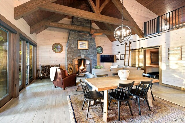 dining space with ceiling fan with notable chandelier, wood ceiling, high vaulted ceiling, light hardwood / wood-style floors, and wood walls