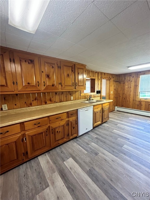 kitchen with white dishwasher, a baseboard heating unit, wood walls, light wood-type flooring, and sink