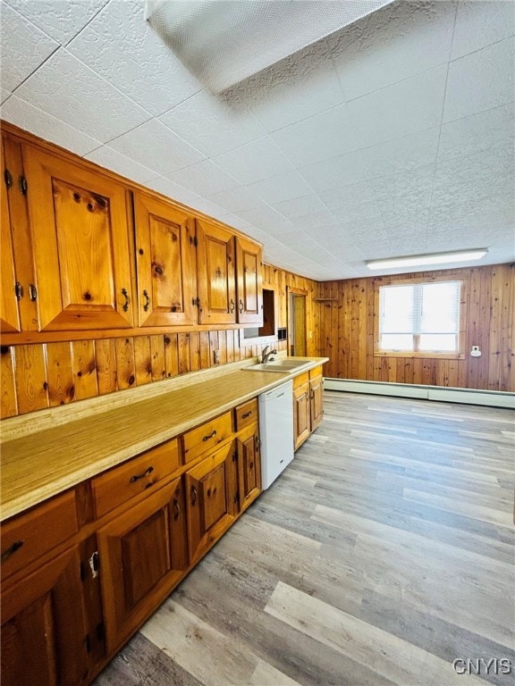 kitchen featuring baseboard heating, light wood-type flooring, wood walls, and white dishwasher