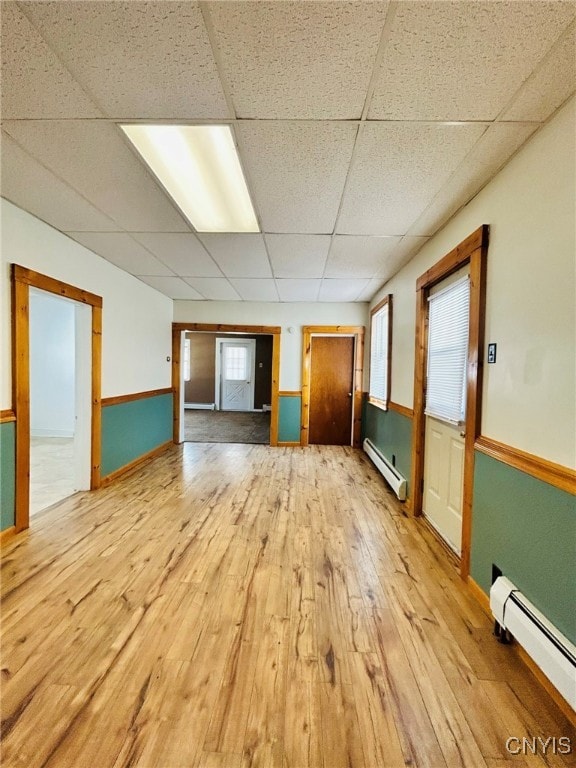 unfurnished room with a baseboard heating unit, a drop ceiling, and light hardwood / wood-style flooring