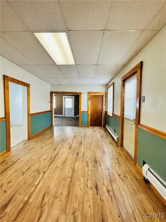 empty room featuring light wood-type flooring, a baseboard heating unit, a drop ceiling, and plenty of natural light