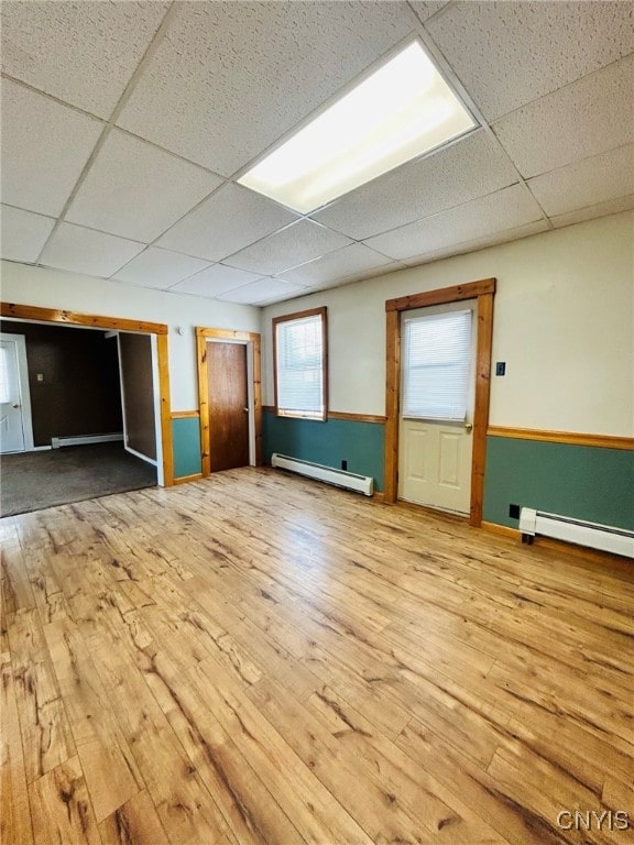 interior space featuring light wood-type flooring, a drop ceiling, and a baseboard radiator