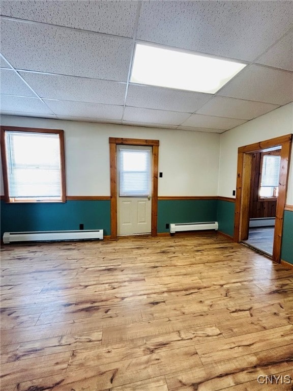 spare room featuring light wood-type flooring, a baseboard heating unit, and a drop ceiling