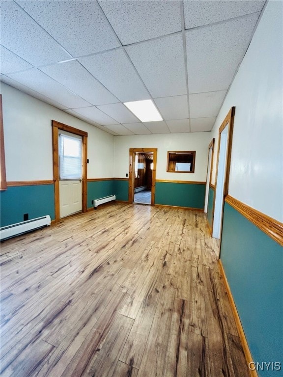 unfurnished room with baseboard heating, wood-type flooring, and a paneled ceiling