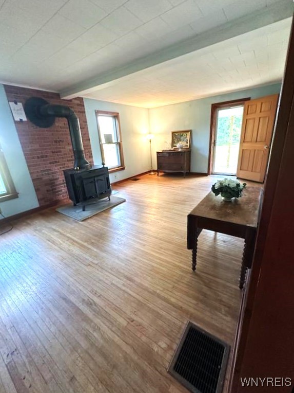 living room featuring beam ceiling, light hardwood / wood-style flooring, and a wood stove