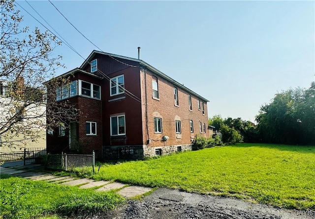 view of side of home featuring a yard, brick siding, and fence