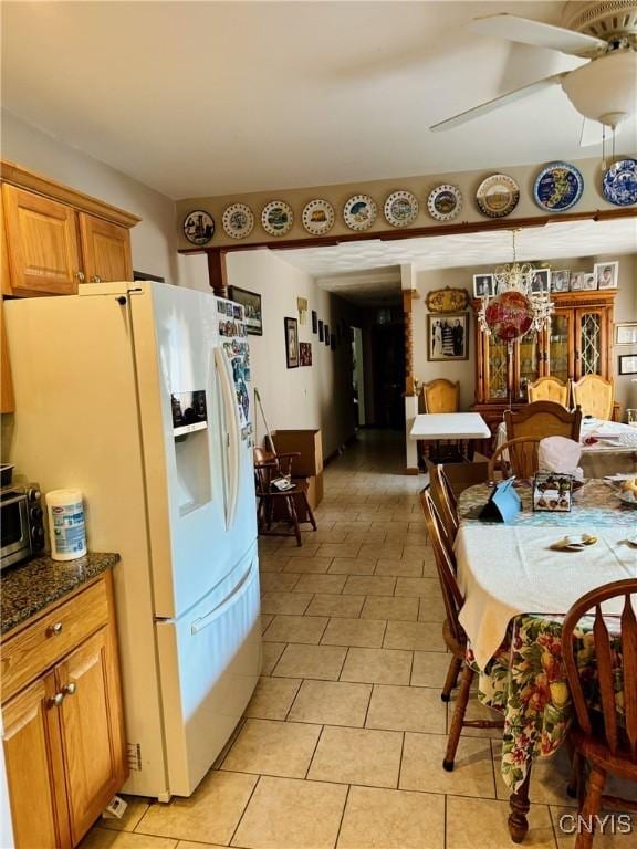 kitchen with light tile patterned floors, a ceiling fan, brown cabinets, dark stone countertops, and white fridge with ice dispenser