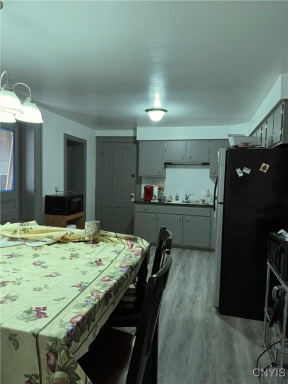 kitchen featuring gray cabinetry, a sink, light wood-type flooring, freestanding refrigerator, and tasteful backsplash