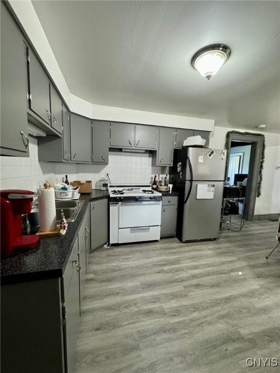 kitchen with gray cabinetry, white range with gas cooktop, freestanding refrigerator, tasteful backsplash, and dark countertops