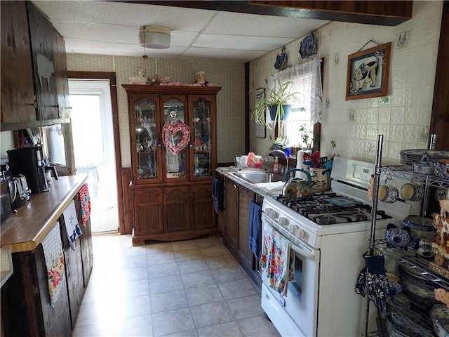 kitchen with light tile patterned flooring, a paneled ceiling, sink, and white gas stove