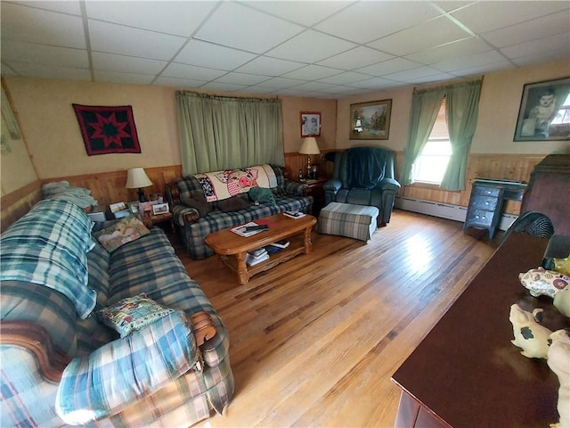 living room featuring wooden walls, a drop ceiling, hardwood / wood-style floors, and a baseboard heating unit