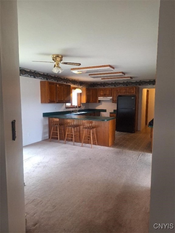 kitchen with light carpet, black fridge, sink, a kitchen bar, and kitchen peninsula