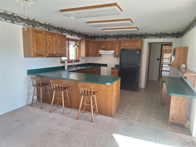 kitchen featuring kitchen peninsula, black refrigerator, light colored carpet, and sink