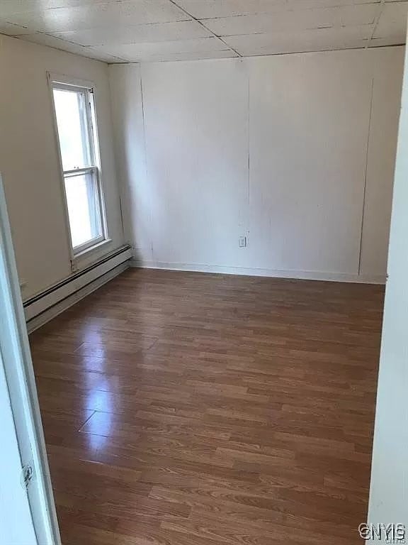 empty room featuring baseboard heating and wood-type flooring