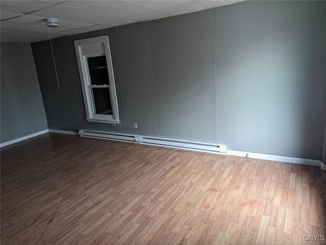 unfurnished room with hardwood / wood-style flooring, a baseboard radiator, and a drop ceiling