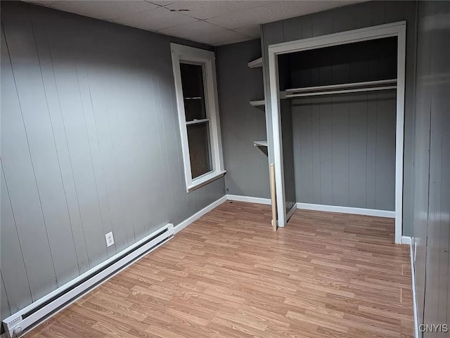 unfurnished bedroom with a closet, a baseboard heating unit, a drop ceiling, and light hardwood / wood-style floors