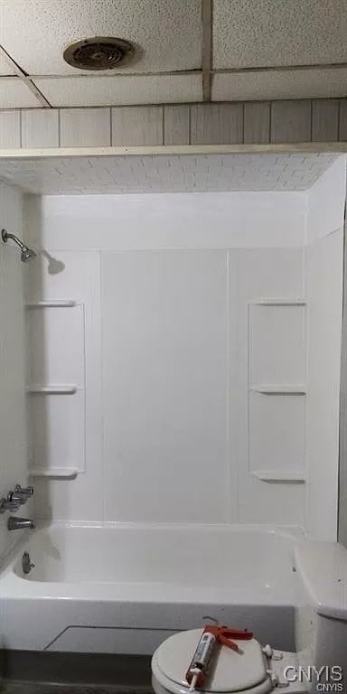 bathroom with shower / bath combination, a drop ceiling, and toilet