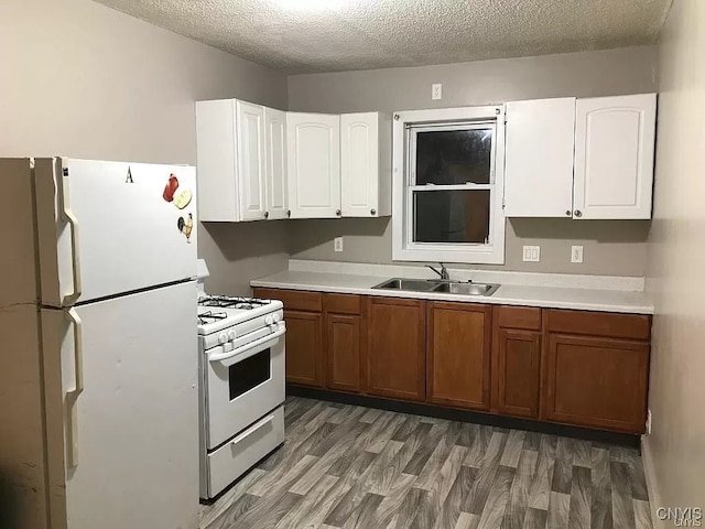 kitchen with a textured ceiling, hardwood / wood-style floors, white cabinets, white appliances, and sink