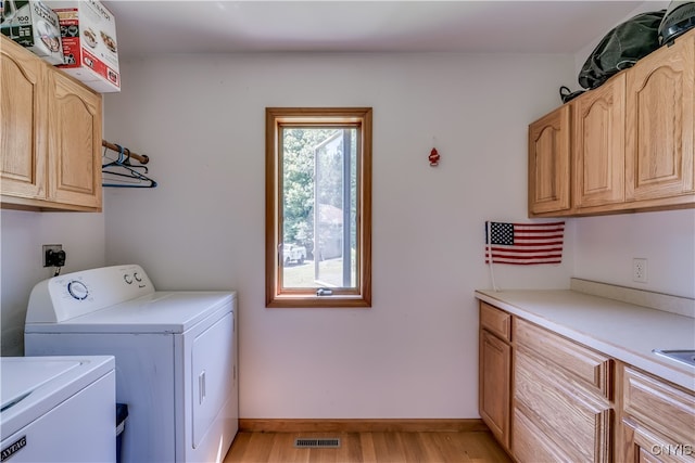 laundry area featuring cabinets, a healthy amount of sunlight, washing machine and clothes dryer, and light hardwood / wood-style floors