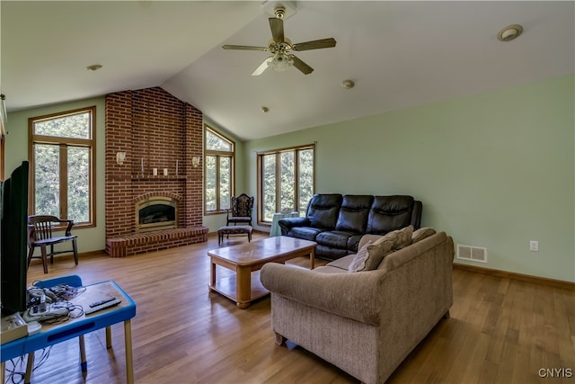 living room featuring lofted ceiling, a brick fireplace, ceiling fan, light hardwood / wood-style flooring, and brick wall