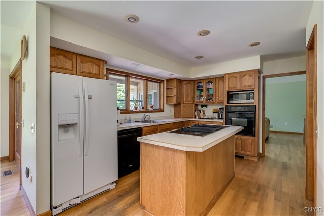 kitchen featuring sink, light wood-type flooring, a kitchen island, and black appliances