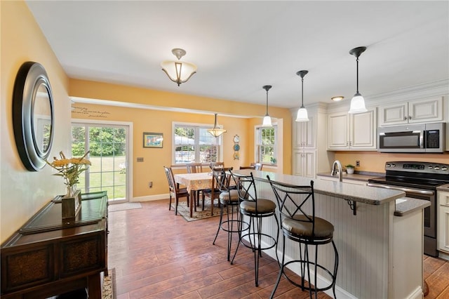 kitchen with dark wood-type flooring, a breakfast bar, appliances with stainless steel finishes, hanging light fixtures, and light stone counters