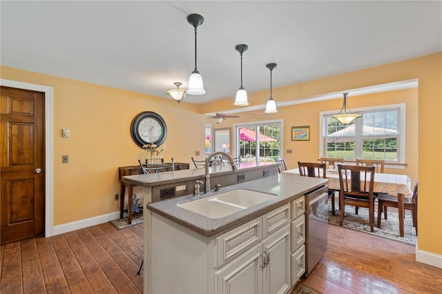 kitchen featuring dark wood-type flooring, sink, decorative light fixtures, stainless steel dishwasher, and an island with sink