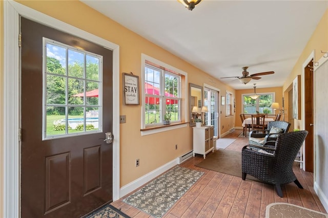 doorway with ceiling fan, wood-type flooring, a wealth of natural light, and a baseboard heating unit