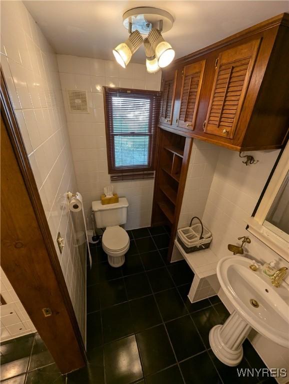 half bath featuring tile patterned flooring, toilet, and tile walls