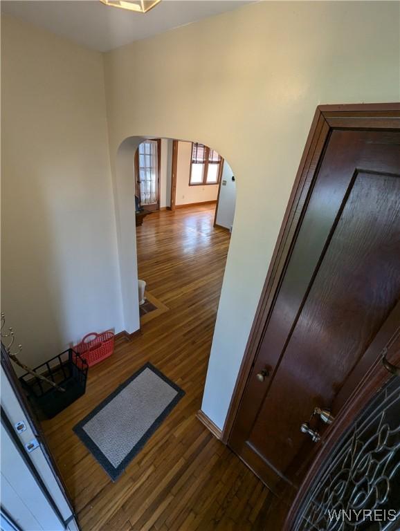 stairs with arched walkways, wood finished floors, and baseboards