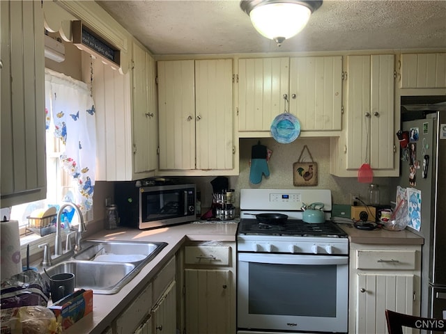 kitchen with sink, a textured ceiling, cream cabinets, and gas range oven