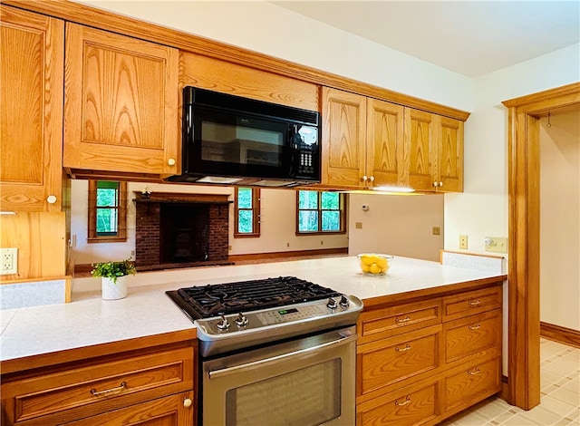 kitchen with kitchen peninsula, gas range, a brick fireplace, and a healthy amount of sunlight