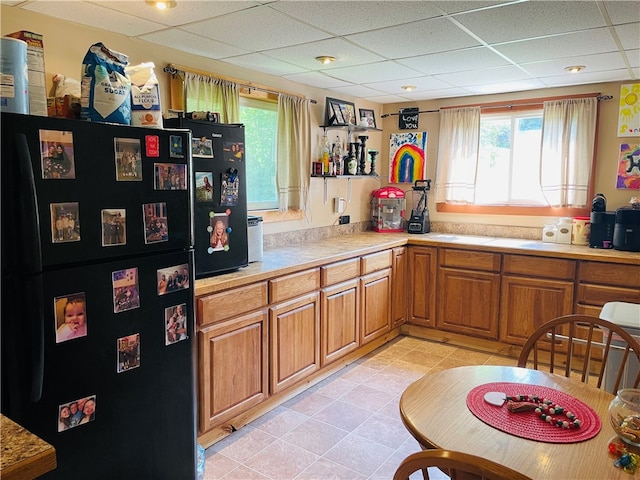 kitchen with light tile patterned flooring, black refrigerator, and a drop ceiling