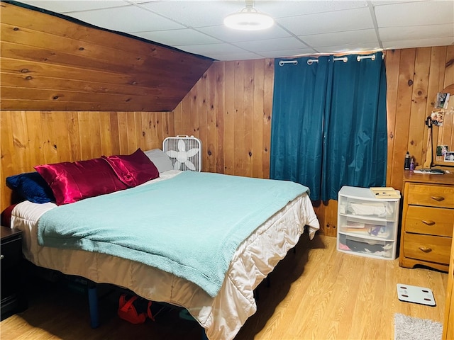 bedroom featuring a drop ceiling, wooden walls, light wood-type flooring, and lofted ceiling