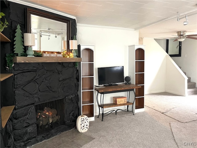 carpeted living room featuring a stone fireplace, ceiling fan, rail lighting, and ornamental molding