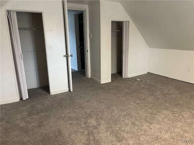 unfurnished bedroom featuring dark carpet, lofted ceiling, and two closets