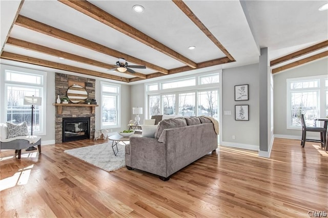 living room with light hardwood / wood-style flooring, ceiling fan, a stone fireplace, and beamed ceiling